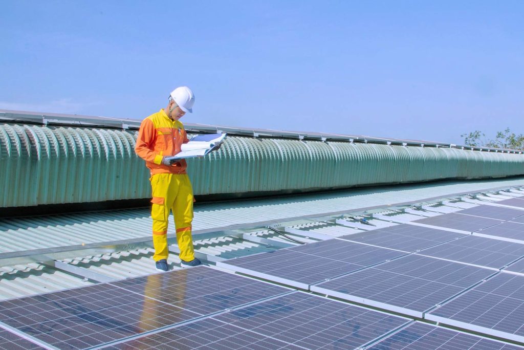 A solar engineer inspects panels on a factory roof