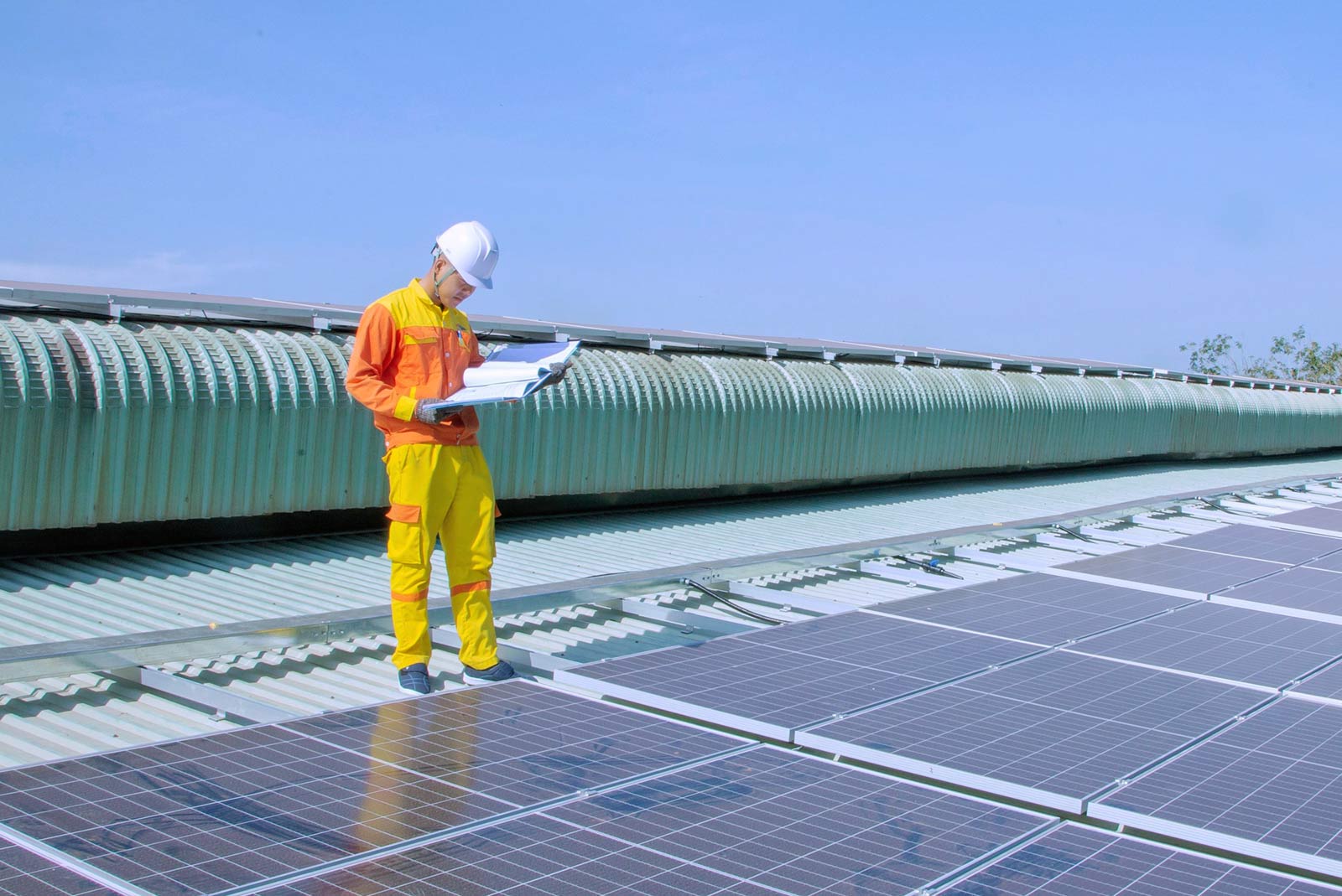 A solar engineer inspects panels on a factory roof